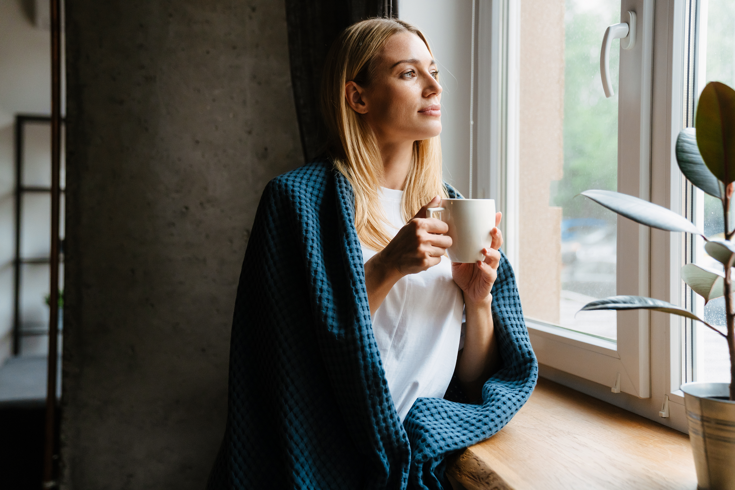 Woman with cover looking out the window with coffee cup